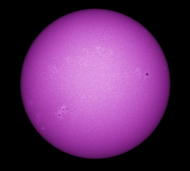 Purple disk view of the Sun's chromosphere featuring darker spots called sunspots and phages, or lighter clouds, across the visible section of the Sun.