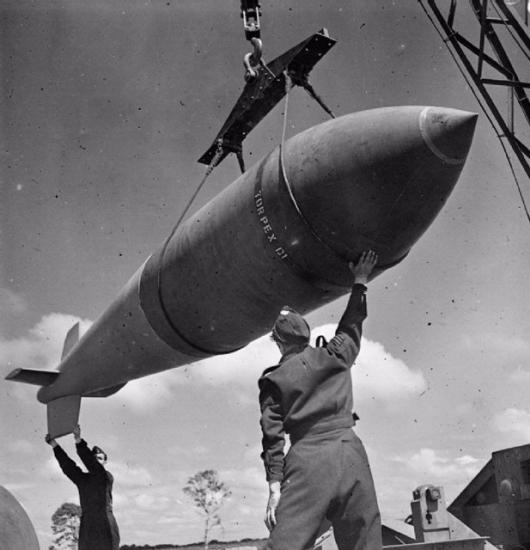 Two men assist in hoisting a large bomb shaped like a missile.