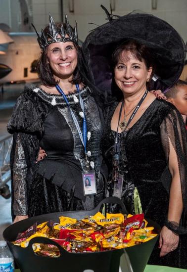 Two women wearing Halloween costumes pose behind a dish of candy at the Museum's annual Halloween event.