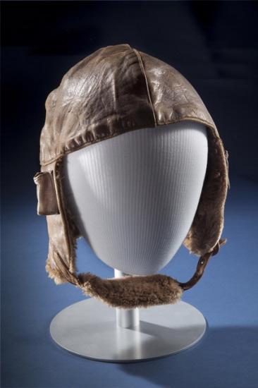 Brown leather aviation helmet with brown fur-lined chin strap. Styled on mannequin.