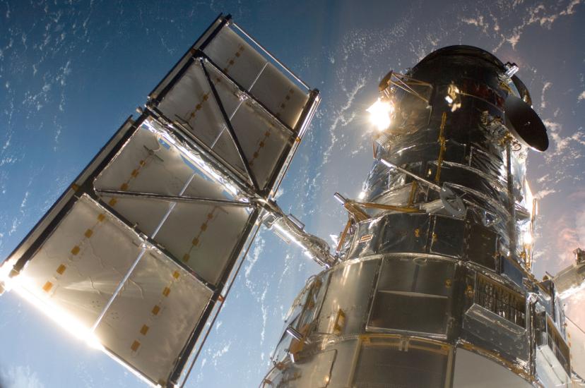 Partial view of the Hubble Space Telescope, a large telescope with two sets of solar panels (one on each side), from the perspective of the Space Shuttle Atlantis.