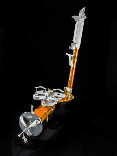 Orange and silver-colored L-shaped object with two restraints meant to hold a single foot during a spacewalk. On both ends, there is a single attachment site.