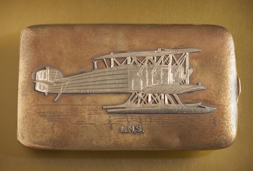 Top of golden box-shaped case featuring an engraved golden biplane.