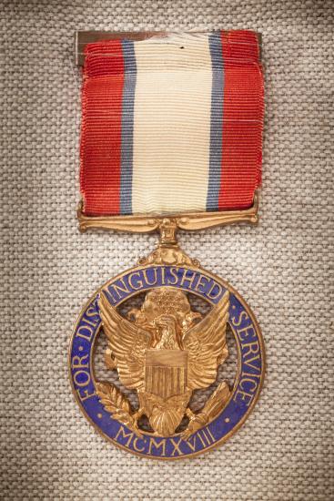 Purple and gold-colored metal medal with red, white, and blue-stripped ribbon. Front of medal features an eagle crest.