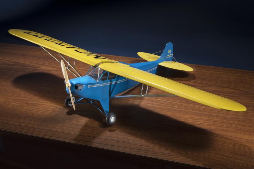 Diagonal front view of blue and yellow monoplane model with one engine represented by a wooden set of two blades.