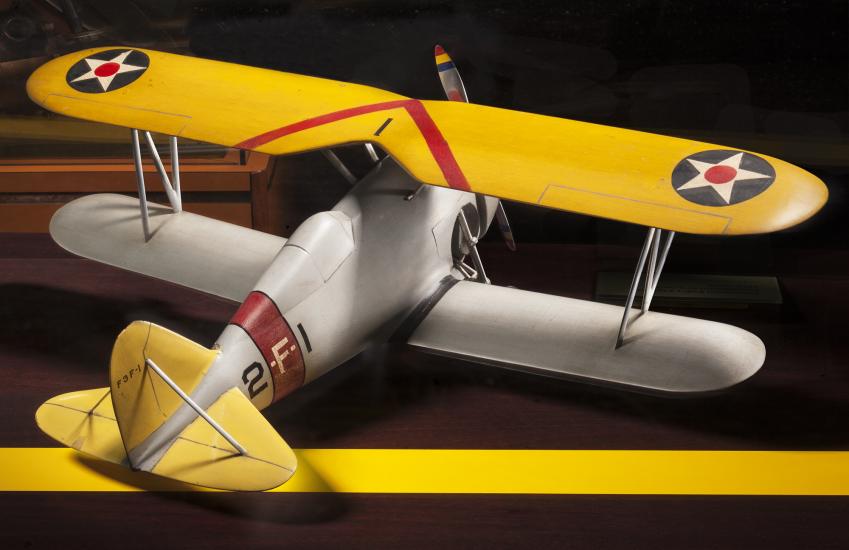 Back view of yellow and silver-colored biplane model aircraft. One white star inside a blue circle is featured on both sides of the top wing.