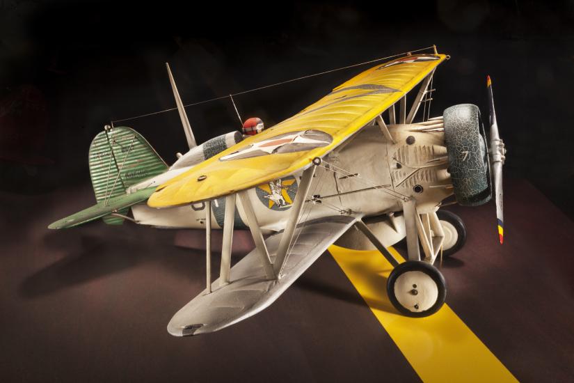 Side view of tan brown and yellow biplane model aircraft with one engine. 