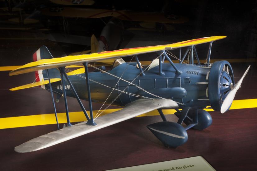 Side view of gray biplane model aircraft with yellow and silver-colored wings and one propellor.