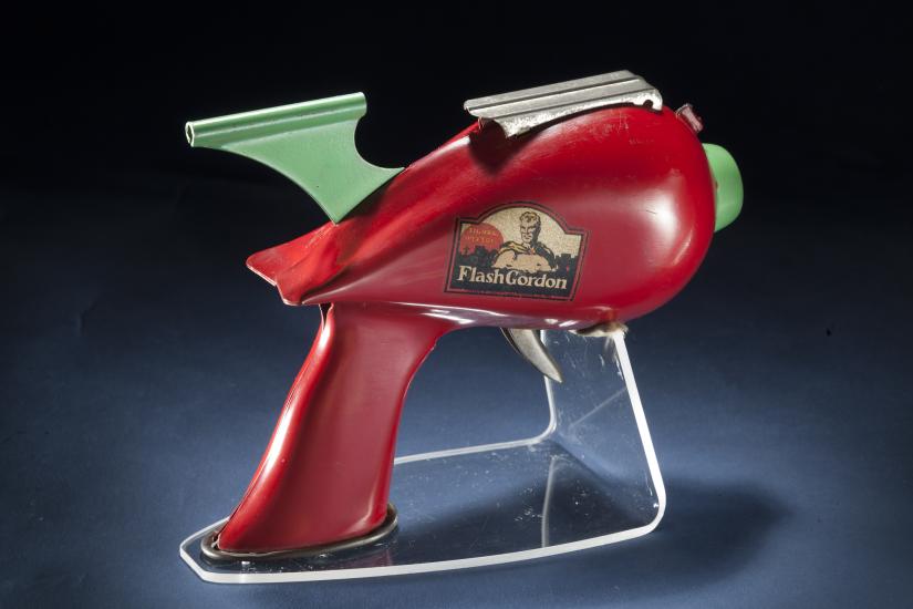 Side view of red-colored steel gun toy with light green trigger. Flash Gordon logo on the middle of the toy.