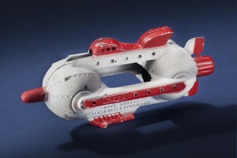 Side view of white attacking spaceship toy with center opening between two spherical sides of the ship. Ship features red fins, nose, and propellor.