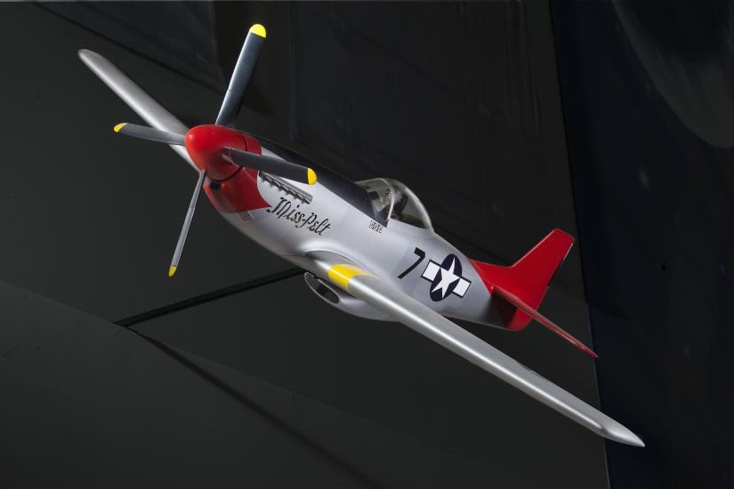 Frontal side view of silver-colored monoplane model aircraft with one engine and a red tail and nose. Blue and white star emblem is painted on the rear of the fuselage.