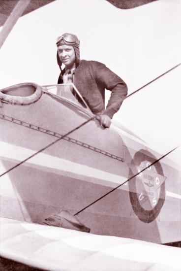 Earl W. Renfroe, an African-American male pilot, stands in the cockpit of a biplane.