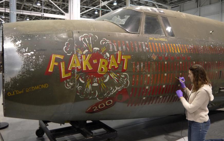 A member of the Museum's conservation staff works to conserve a portion of an olive drab green bomber aircraft from World War II.