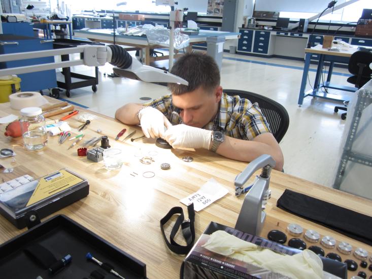 A white, male professional watchmaker closely inspects a watch.