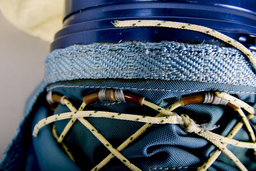 Close-up view of developmental blue glove. Thin, tan rope acts as a lacing system under a blue skirt.