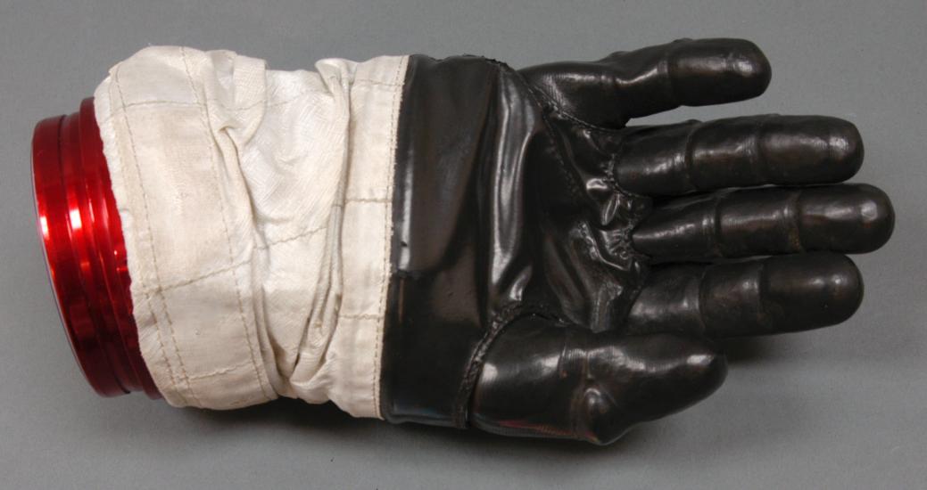 Right glove to astronaut suit. Black-colored rubber palm and fingertips section attached to a white fabric. The white fabric is attached to a solid red disconnect from the rest of the suit.