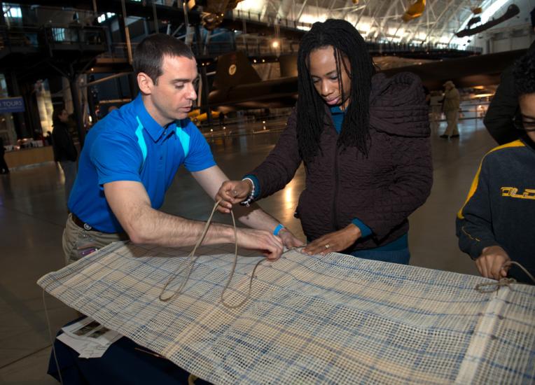 A Museum staff member assists two Museum visitors with activities at a table during an open house event.