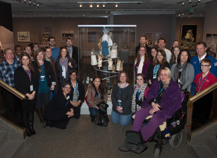 A group of people pose together around an artpiece made from various astronaut gloves.