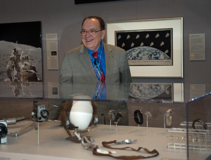 A former NASA manager for astronaut hardware and shuttle crew accomodations smiles behind a display of small spaceflight related objects.