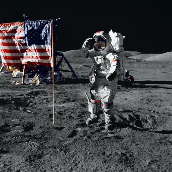 Eugene A. Cernan, a male astronaut wearing a full-body spacesuit, salutes a red, white, and blue U.S. Flag on the surface of the Moon.