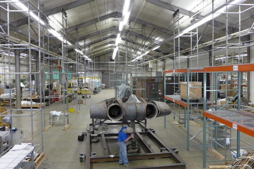 A Museum staff member is securing a gray-colored metal aircraft to a steel stand.