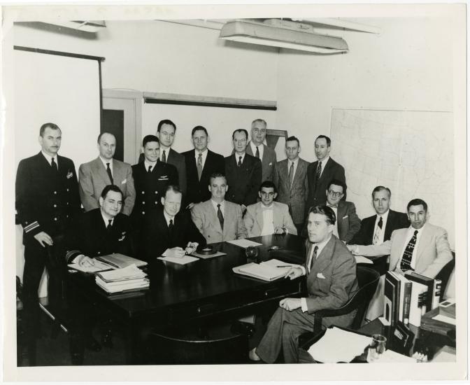 A group of men pose formally during a meeting to discuss spacecraft.