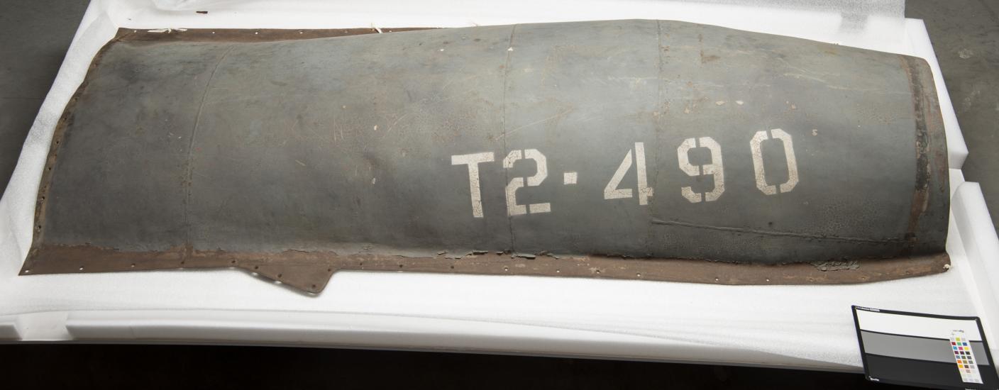 A gray-colored engine cover belonging to a gray military aircraft. The engine cover features the marking "T2-490" on the right side of the visible cover.