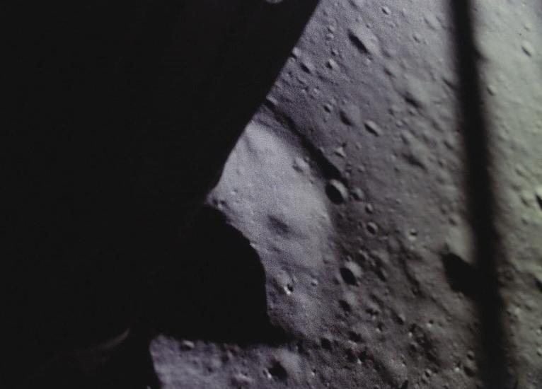 Partial view of the Moon's surface taken from a camera mounted on the Lunar Module. The surface features multiple craters.