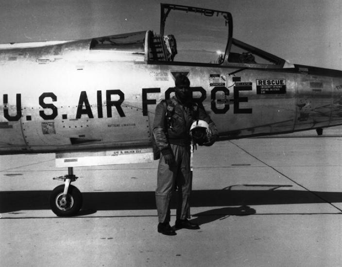 Major Robert Lawrence, an African-American male pilot and pilot, poses outside of an aircraft in aviation gear. He is holding his helmet.