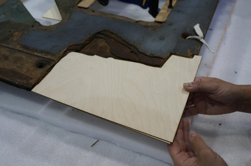 A Museum staff member places a second layer of plywood intended for use in repairing holes in a World War II era aircraft.