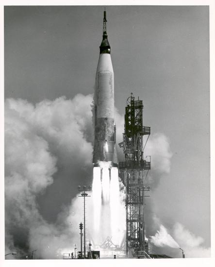 A Mercury-Atlas rocket launching from a launch pad.