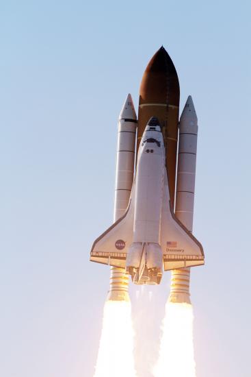 Space Shuttle Discovery, a plane-like object used in space which is attached to three large rockets, is soaring in the atmosphere towards space.