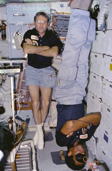 Astronauts Richard Truly and Guy Bluford sleep aboard the STS-8 Challenger mission. Truly sleeps with his head towards the ceiling whereas Bluford is sleeping with his head towards the floor.