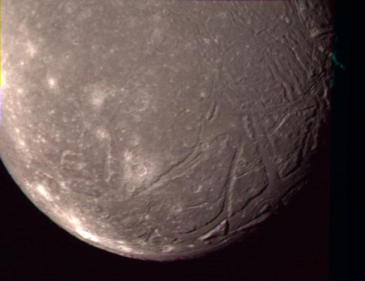 A close-up view of Ariel, a moon of Uranus, and some of its terrain with large craters creating lines