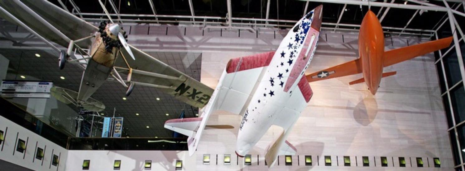 A red, white, and blue rocket-shaped spacecraft with foldable wings displayed inside the National Air and Space Museum.