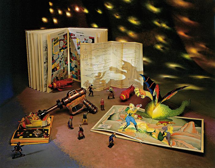 A collection of space-themed toys and comic books on a table with stars projected in the background.