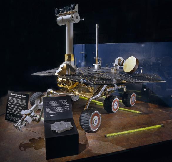 Large spacecraft model with six sturdy wheels, a flat platform covered with solar panels, and a vertical boom with camera on top.