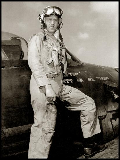 Bill Daniels, a man, stands on the wing of a Grumman F8F Bearcat while wearing aviator gear.