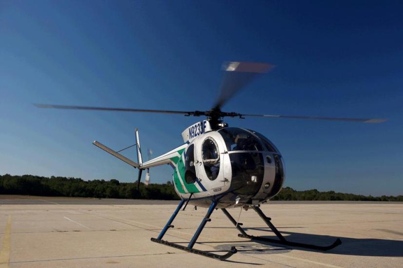 A silver and green helicopter with three propellor blades.