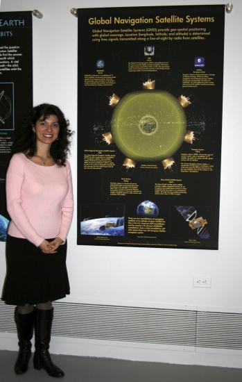 A college student stands to the side of their banner discussing social uses of GPS technology