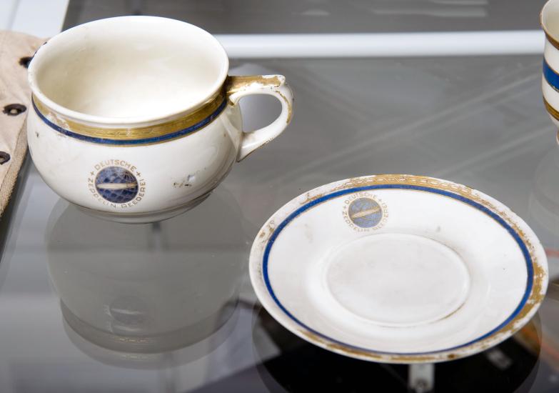 A white cup and saucer, each featuring a small depiction of the Hindenberg airship