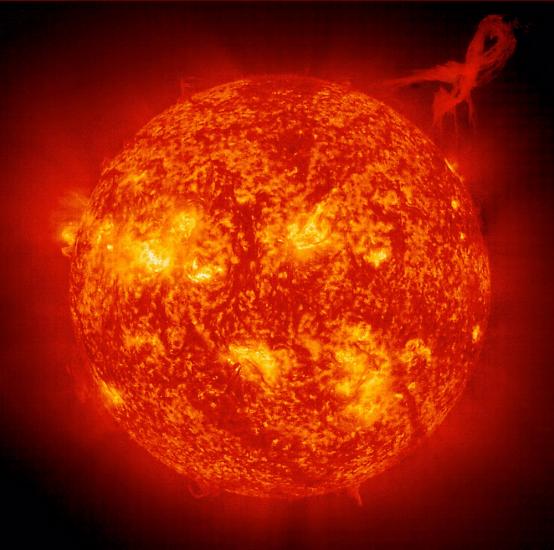 A prominence, a cloud of cool, dense plasma, erupts and escapes the sun's atmosphere in the upper right quadrant of the photo.