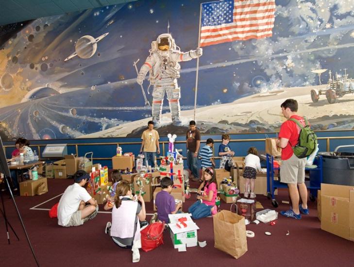 Families work on building pieces of a recycled space station project.