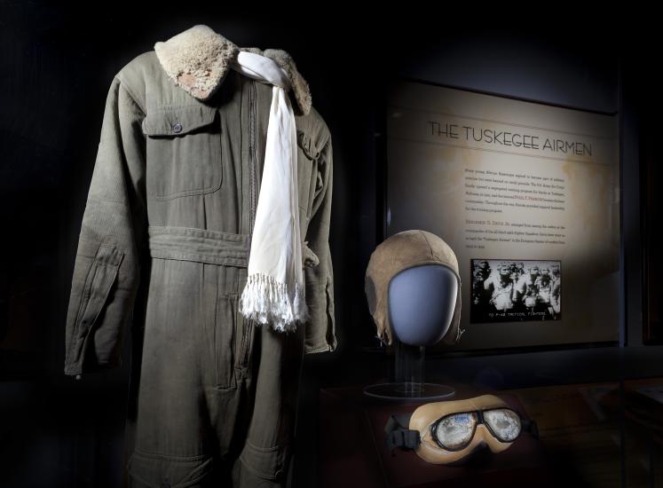 Flight suit, scarf, helmet, and goggles displayed next to Tuskegee Airmen graphic