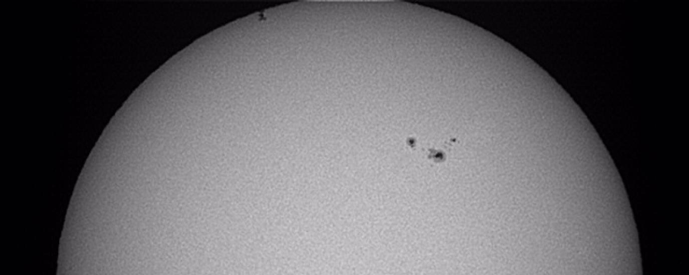 A partial view of the Sun as the International Space Station, a set of dots on the upper left side of the photo, transits the Sun.