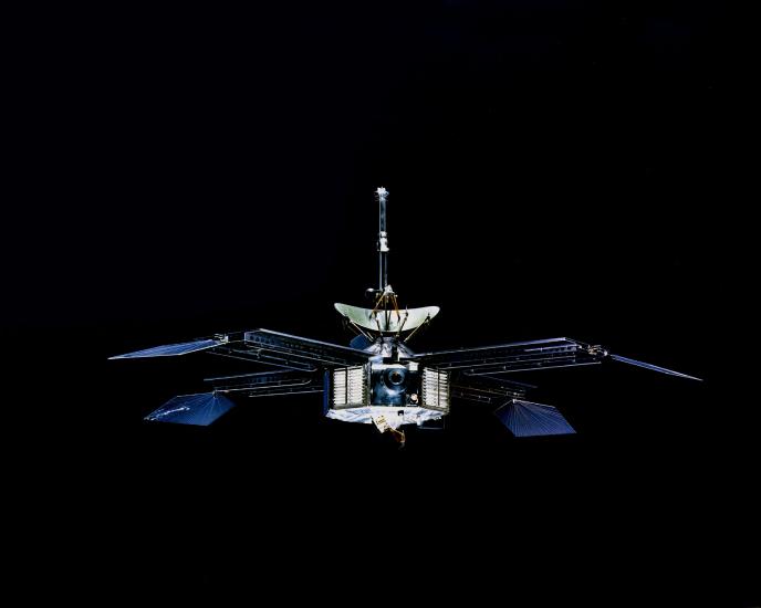 A spacecraft with a hexagonal prism-shaped base and four retractable sets of solar panels. A satellite is pointed above the base.