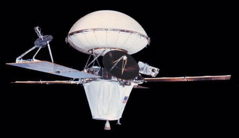 A spacecraft with a uneven cylindrical prism base with four solar panels, a satellite disk, and other items attached to the top of the base. Above the base and other items is a mushroom-shaped cover concealing various sensors used for reconnaisance.