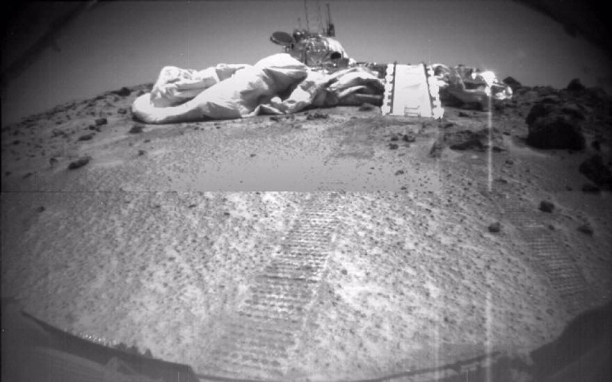 A view of the Mars Pathfinder lander, a set of paths and cushioning tarps designed to land the Sojourner rover on Mars, is passed by the Soujourner rover.