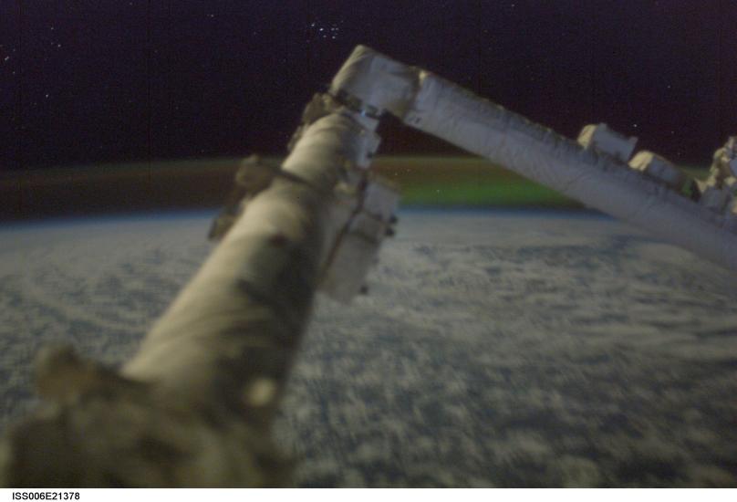 A large, arm-like object on the International Space Station in front of the Aurora Borealis in the background.