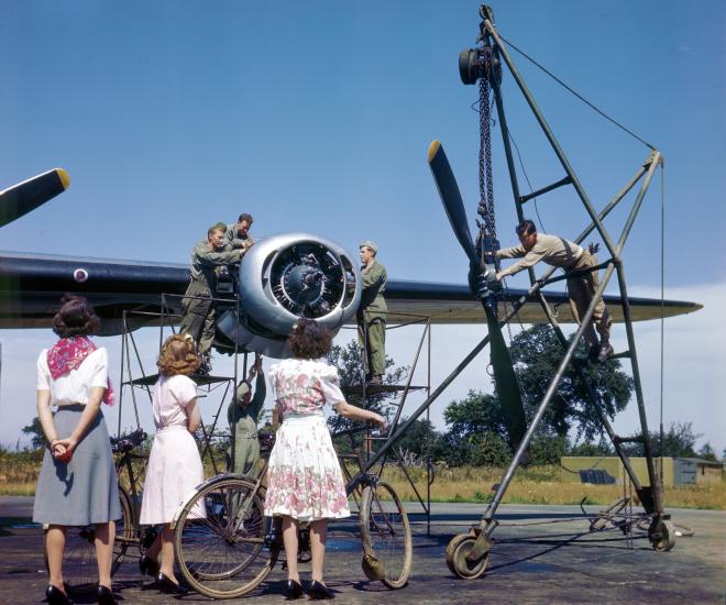 English women watch an Eighth Air Force maintenance crew work on a B-24 engine.